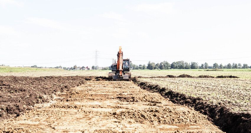 Foto van kraan die bezig is met het omkeren van de veenlaag en de zandlaag